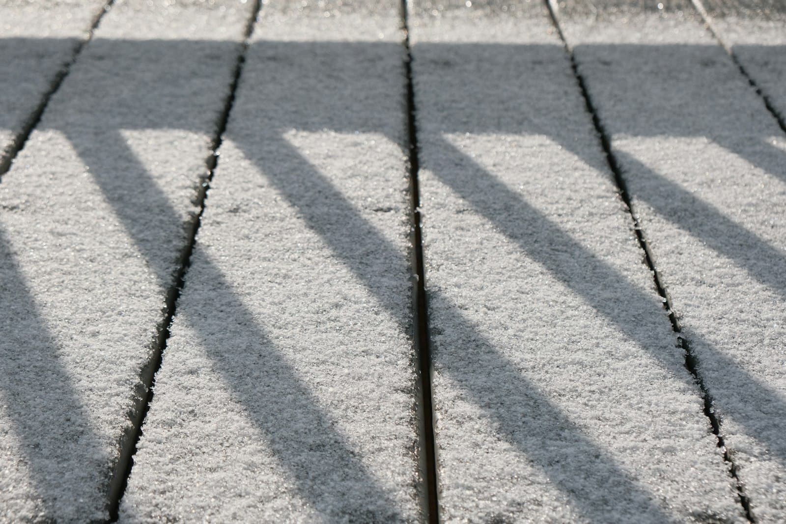 A wooden deck surface dusted with light snow showing the long shadow patterns and lifted board edges typical of southern Ontario freeze-thaw weather.